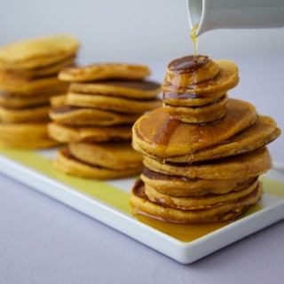 Different sizes of pancake—from silver dollar to 4inch rounds—stacked on a platter syrup drizzling down from above.
