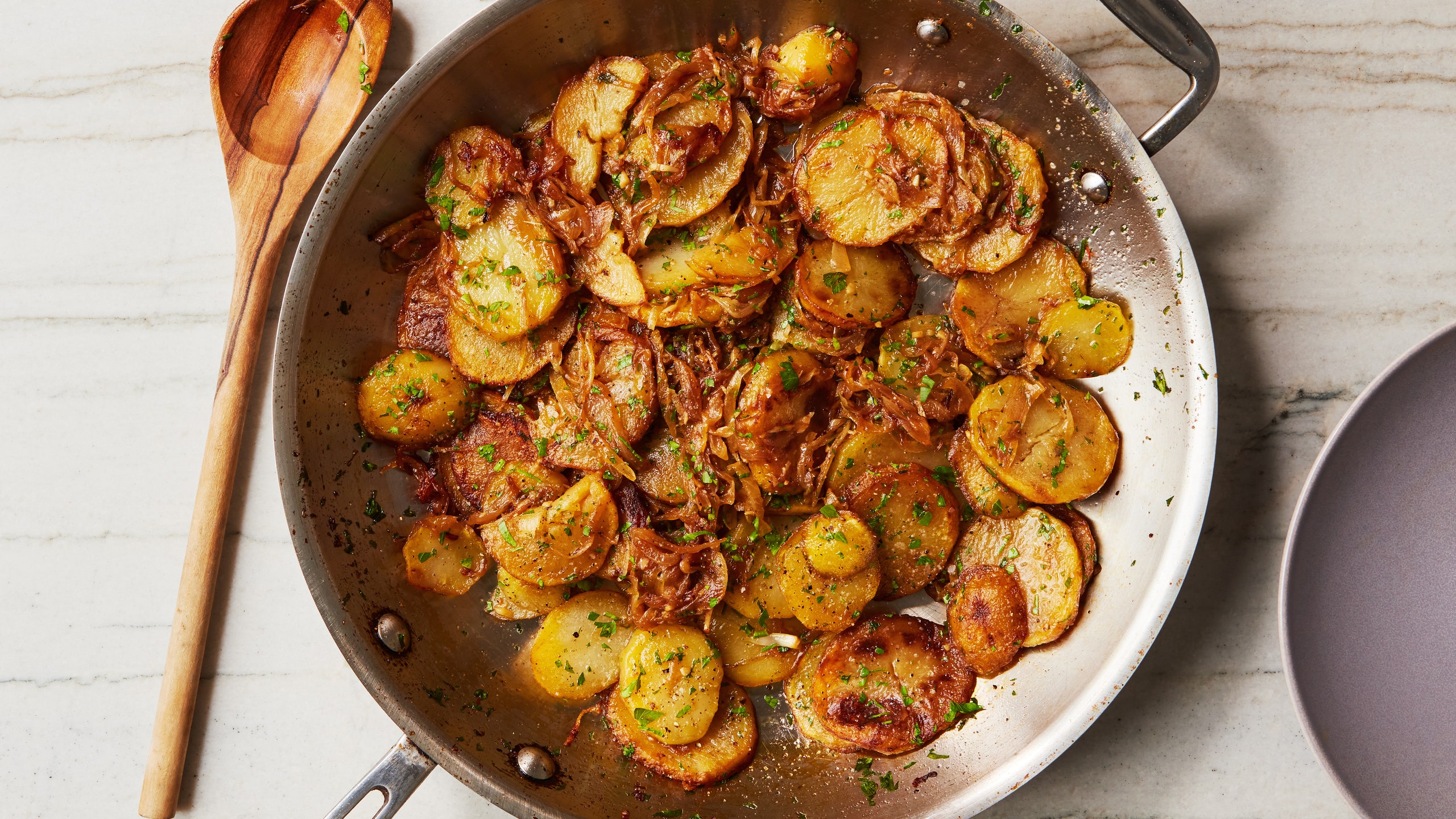Sliced potatoes in a pan with caramelized onions and fresh parsley.
