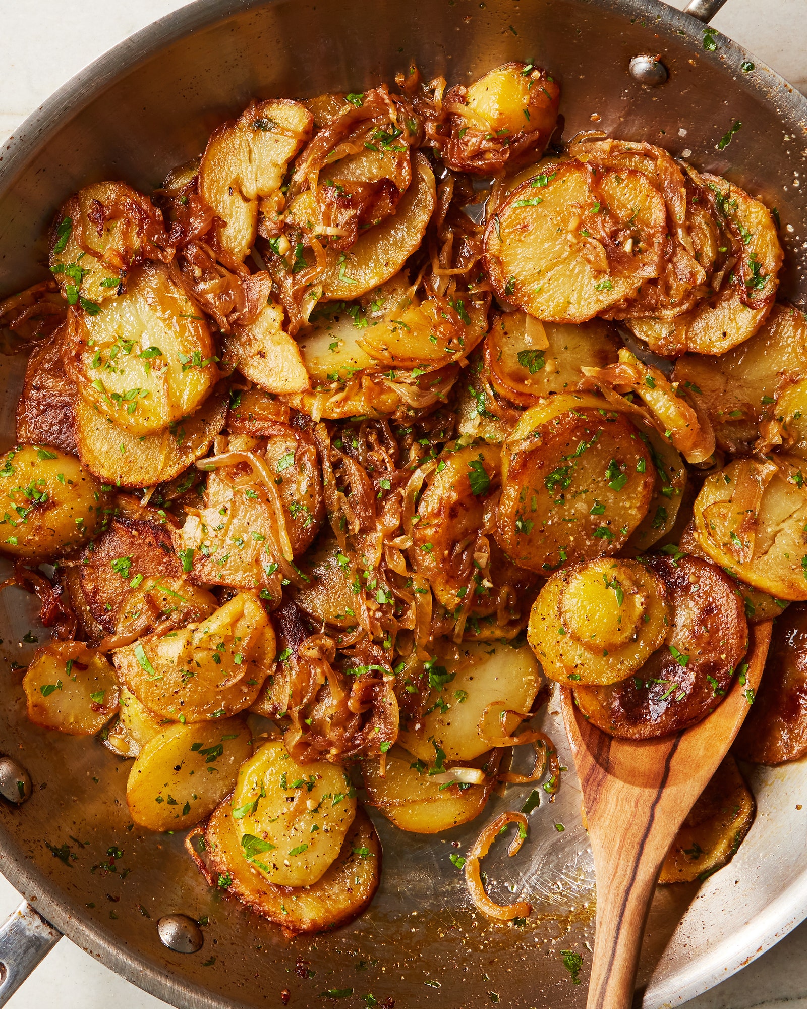 Sliced potatoes in a pan with caramelized onions and fresh parsley.