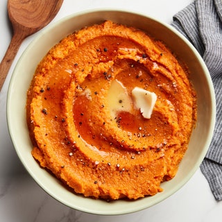 A serving bowl of mashed sweet potatoes with melted butter maple syrup and ground black pepper.