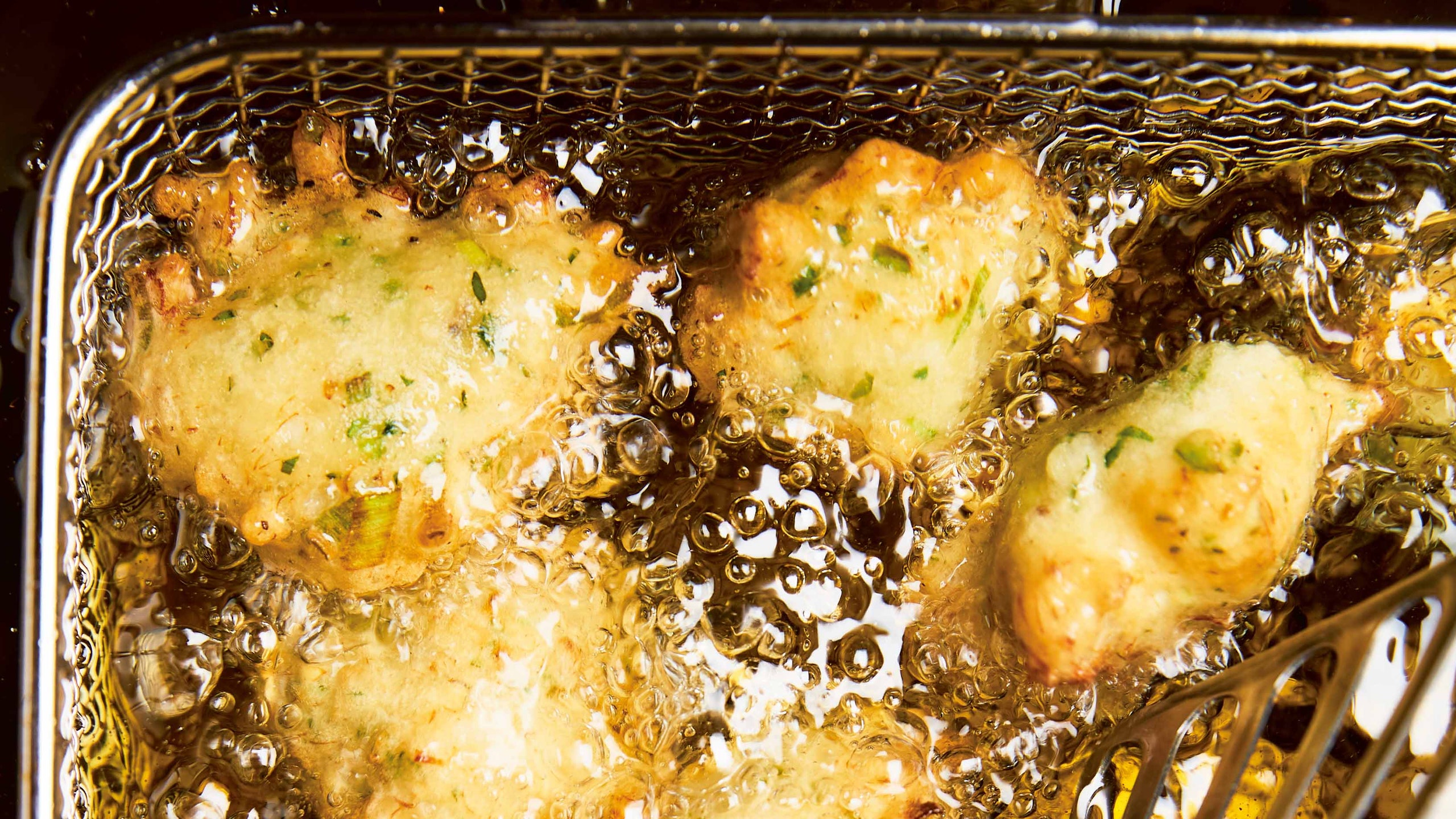 Salt cod fritters frying in a deep fryer with a fish spatula reaching in