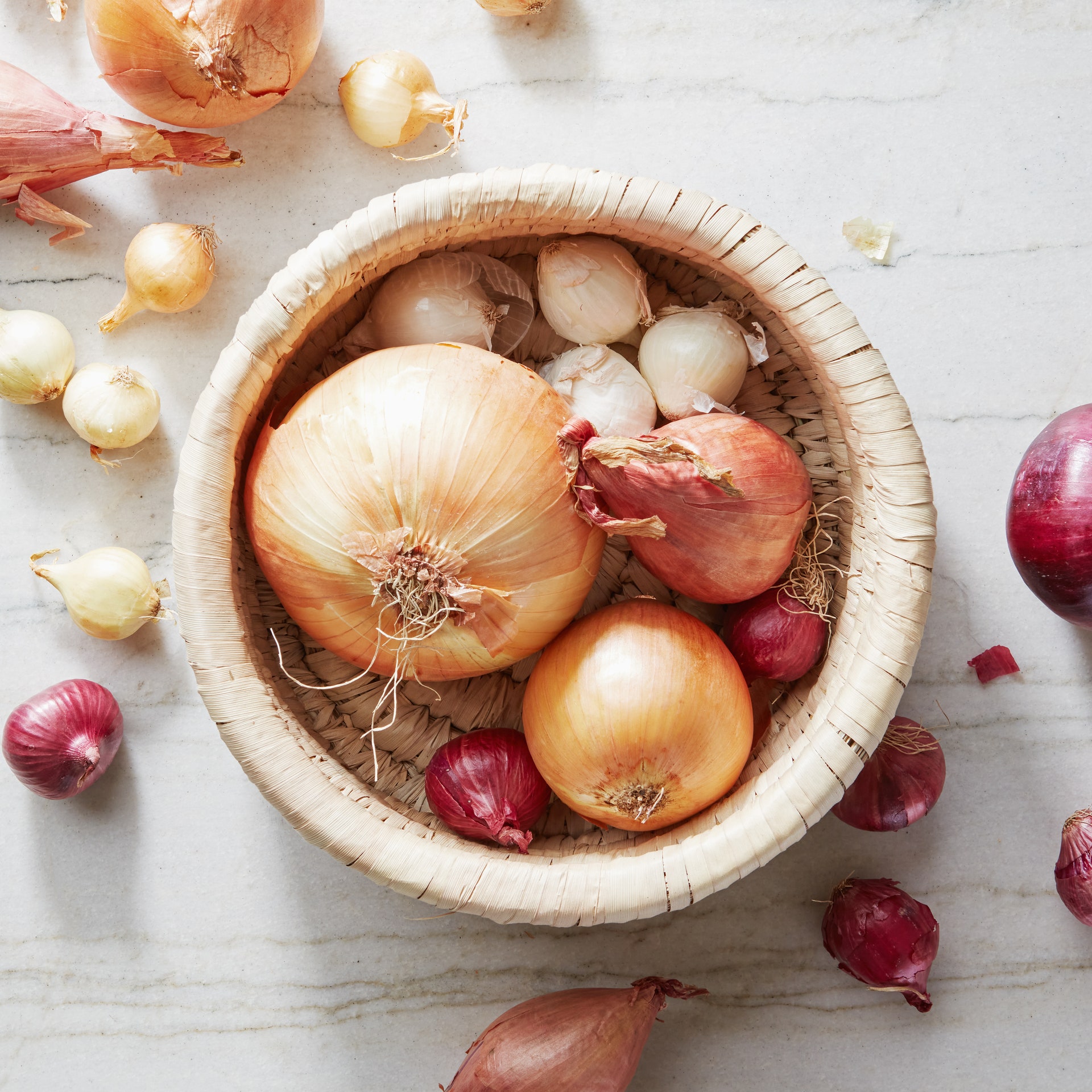 A variety of onions in a basket and on a countertop.